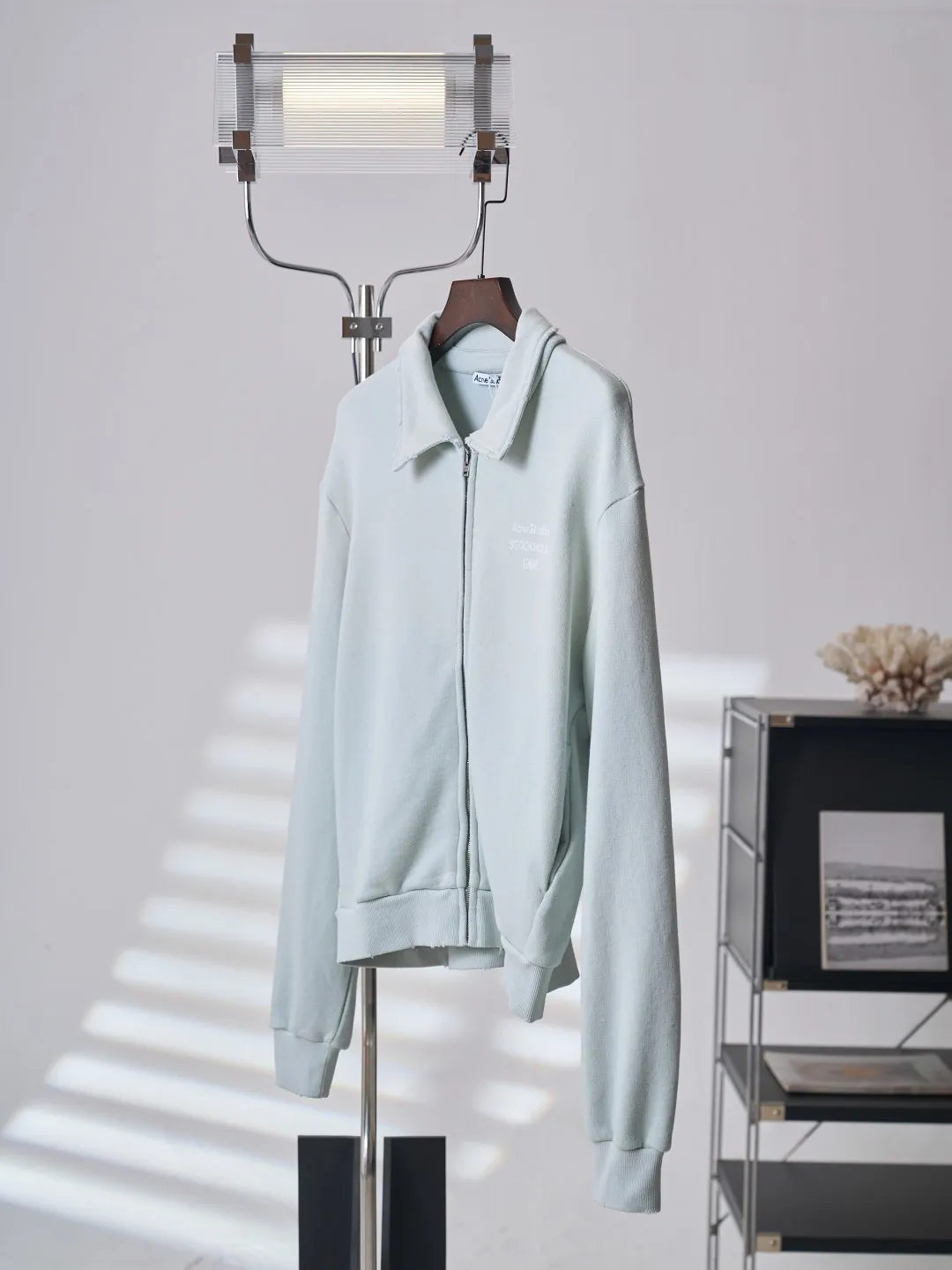 [Real auction] Acne Studios Retro distressed letter print zipper jacket [In Stock] Logo stamp at front, side-seam pockets, and ribbed cuffs and hem. Regular fit, just above the waist. It adopts a 3-strand composite fleece structure with 32 counts for the top layer and 40 counts for the bottom layer, with a weight of g/㎡. The 32-count yarn on the top layer is fine and smooth, giving the surface a smooth touch and excellent anti-pilling properties; the 40-count 3-ply yarn on the bottom layer is treated with a raising process to form a rich and soft fluff layer, providing excellent warmth and skin-friendly wrapping. With 21 2×2 ribs, the g/㎡ weight ensures that the collar, cuffs and hem have excellent tensile fatigue resistance and shape retention capabilities. During piece dyeing, the entire fabric is immersed in the dye vat after weaving, and the dye molecules fully penetrate into the fibers, ensuring full, deep colors and excellent color fastness. Each batch of dyeing produces subtle differences, making the color tone of the single product unique. On this basis, the paint is sprayed irregularly on the surface of the garment through manual spray painting to create a splash-like retro effect. The distressed processing of holes causes the color to fade and mottle in parts. The ribbed trim is also treated to form slight whitening and fluffing, which visually echoes the spray-painted effect on the body, making the new clothes appear as if they have been worn for a long time and exposed to the sun. The front logo stamp uses a slurry printing process. The printing slurry contains a special microcapsule foaming agent. After being baked at high temperature, the slurry layer expands to form three-dimensional bulges, and the surface presents a granular texture similar to inkjet paint. This process simulates the effect of random drops of pigment after being atomized during spray gun spraying. The edges of the pattern present a natural feathering transition, rather than the rigid boundaries of glue printing. The printing surface has a fine graininess and soft elasticity to the touch, forming a closed loop of the process with the distressed effect of the spray painting on the body.